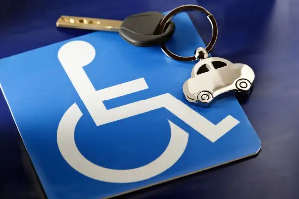 Chiave e portachiavi a forma di auto su un cartello blu con simbolo di disabilità. Possibile riferimento a invalidità civile 75 e bollo auto.