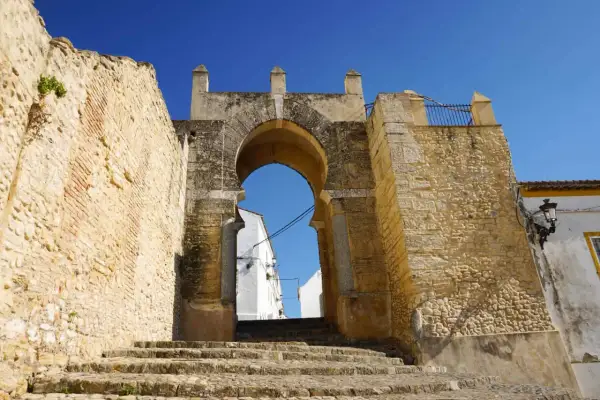 Antigua puerta de acceso a Medina Sidonia, con escalinata de piedra y cielo azul. Merece la pena visitar Medina Sidonia.