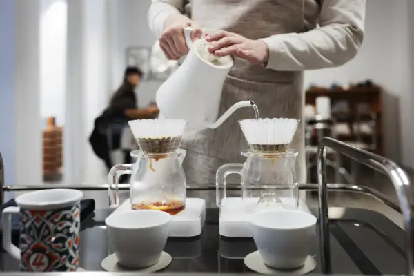 En person häller varmt vatten över kaffefilter för att brygga kaffe. En tanke på vad kostar en kopp kaffe hemma.