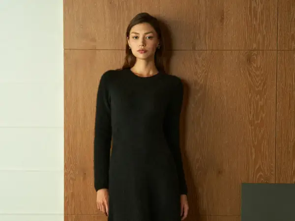Frau in schwarzem Strickkleid vor Holzvertäfelung. Ein schlichtes Outfit, das zu den modernen Dresscodes für Frauen passt.