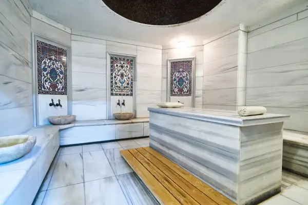 Wnętrze hammamu: marmurowe ściany, ozdobne kafelki, kamienne misy i ława. To miejsce relaksu i odnowy, gdzie poczujesz się jak w orientalnej łaźni.