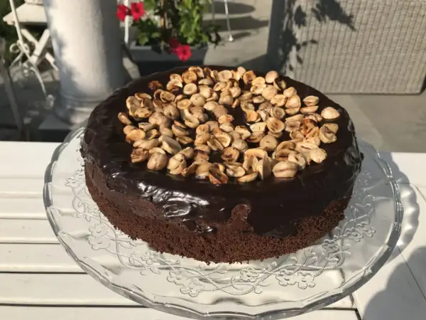 Czekoladowy tort z polewą i orzechami na szklanej paterze.