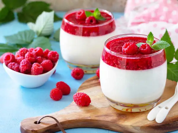Deux panna cotta framboise, garnies de fruits rouges frais et de menthe, sur un plateau en bois.