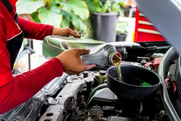 Mecánico vierte aceite nuevo en el motor de un coche, recordando que el aceite de coche caduca y debe cambiarse.