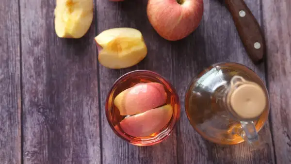 Ein Glas mit Apfelschnitzen und eine Flasche Apfelessig stehen bereit. Zeit, Apfelessig zu trinken!