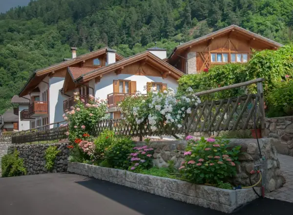 Case con balconi in legno e fiori colorati, incorniciate da un giardino rigoglioso. Un angolo di pace nel Val di Sole, dove si trova questo incantevole paesaggio.