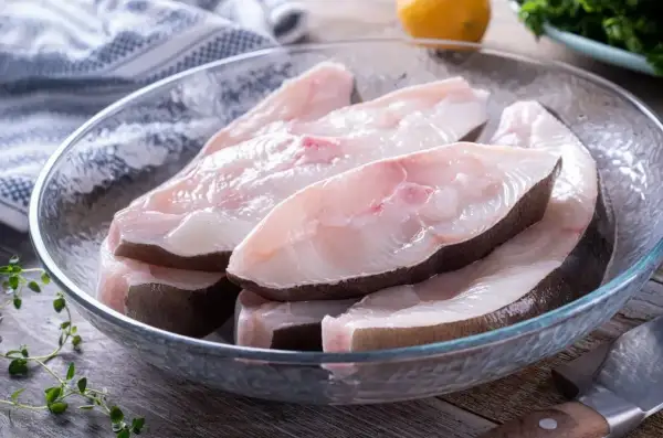 Świeże kawałki halibuta ryby w szklanej misce, gotowe do przygotowania.