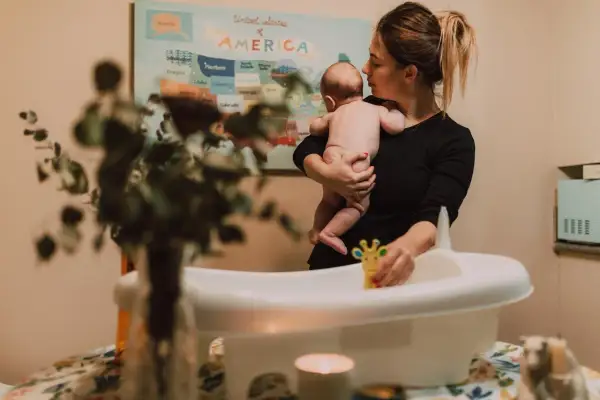 Mamma håller sitt barn redo för att bada. En leksak i form av en giraff ligger i badkaret.