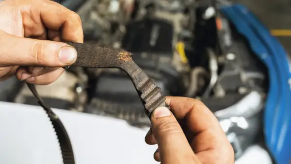 Zużyty pasek rozrządu, który wymaga wymiany, w rękach mechanika.