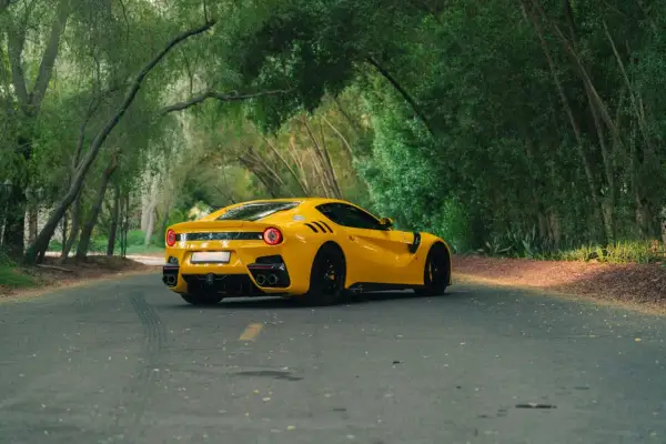 Żółte Ferrari F12 TDF sunie po leśnej drodze, otoczone bujną zielenią.