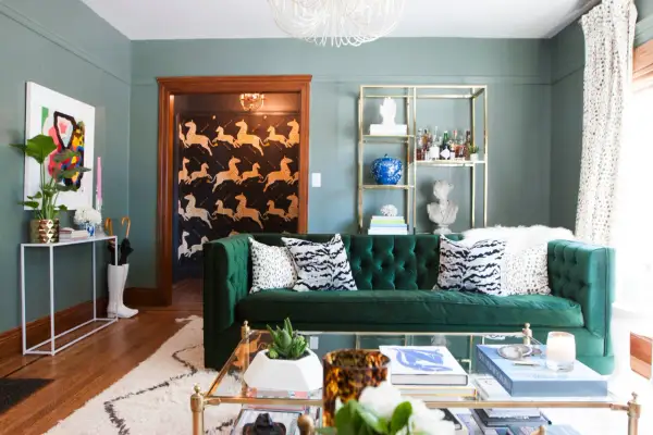 A plush emerald green sofa anchors this living room, featuring a bold zebra print wallpaper in the entryway of this 1920s craftsman house.