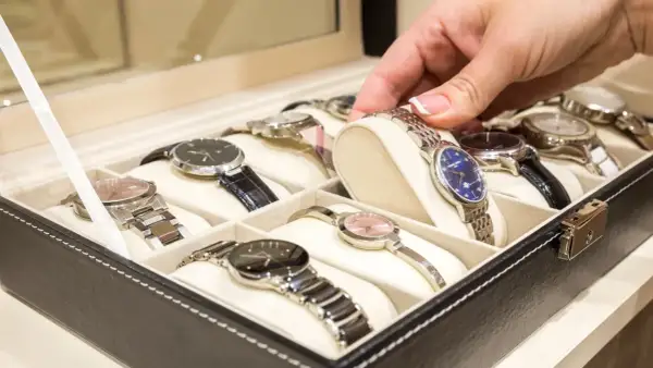 Una mano elige un reloj de una caja. Los relojes de pulsera, algunos de niquel que no se oxida, están ordenados en compartimentos.
