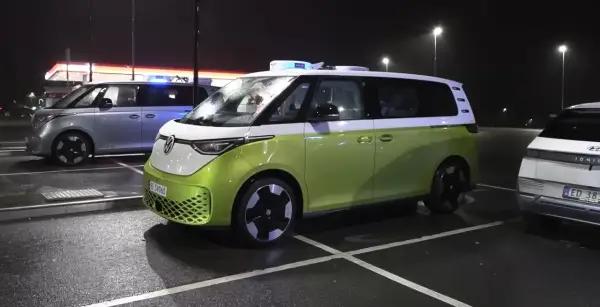 Zielony i srebrny VW ID. Buzz, jeden z niebieskimi światłami, parkuje nocą. Zasięg tych elektryków jest imponujący.