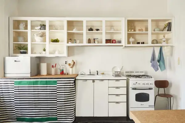 A cozy kitchen with open shelving displaying decorative items. A striped curtain hides the dishwasher, showcasing clever rental friendly upgrades.