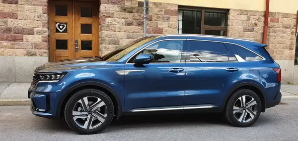 Blå laddhybrid diesel Kia Sorento parkerad framför en tegelbyggnad med en trädörr med ett hjärta.
