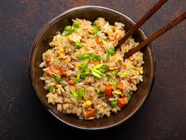 Un piatto fumante di riso alla cantonese ricetta originale, con piselli, carote, uova e cipollotto fresco, pronto per essere gustato con le bacchette.
