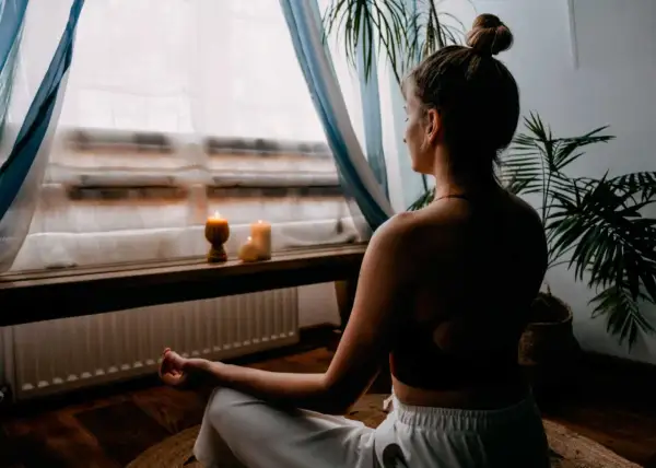 Mujer meditando en un espacio para meditar en casa, con velas encendidas y plantas.