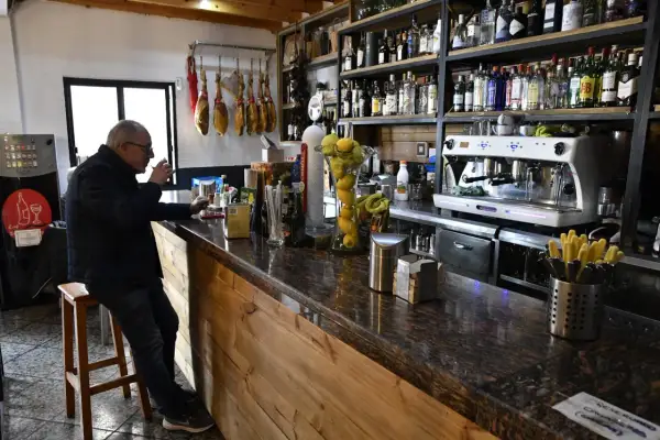 Hombre en taburete en bar Almería Enix, con jamones colgados y estanterías llenas de licores.