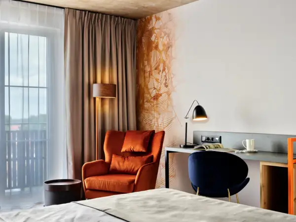 Przytulny pokój w **Bergo Hotel Szklarska Poręba**: pomarańczowy fotel, biurko z lampką i granatowe krzesło.