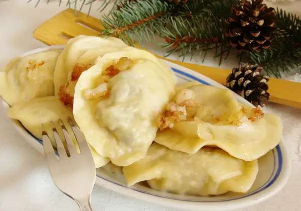 Pyszne pierogi z mięsem i kapustą, okraszone skwarkami, na talerzu z gałązką sosny i szyszkami.