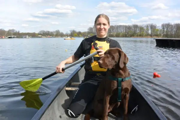 Frau und brauner Hund genießen das Kanufahren mit Hund auf einem sonnigen See.