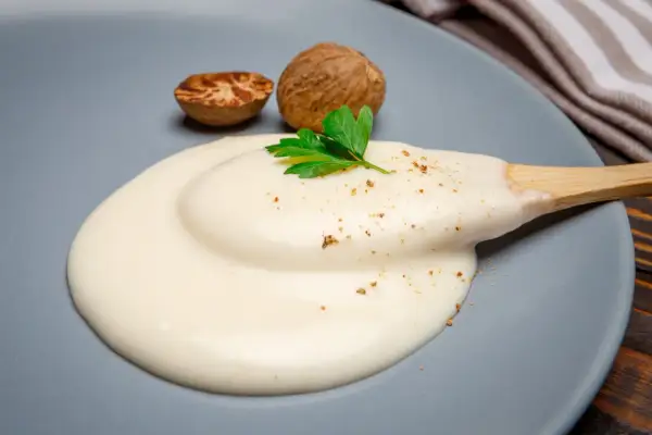 Krämig bechamelsås på en tallrik, med muskotnötter och persilja. Perfekt för att frysa in och använda senare.