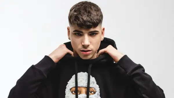 Giovane rapper italiano con un taglio di capelli alla moda, indossa una felpa nera con un disegno artistico.