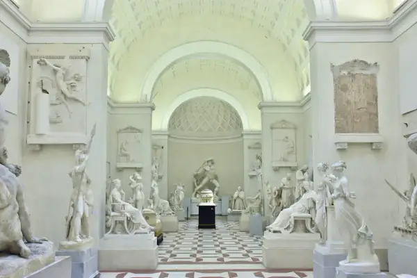 Interno della Galleria dell'Accademia con sculture classiche in marmo bianco, pavimentazione a scacchi e soffitto a volta.