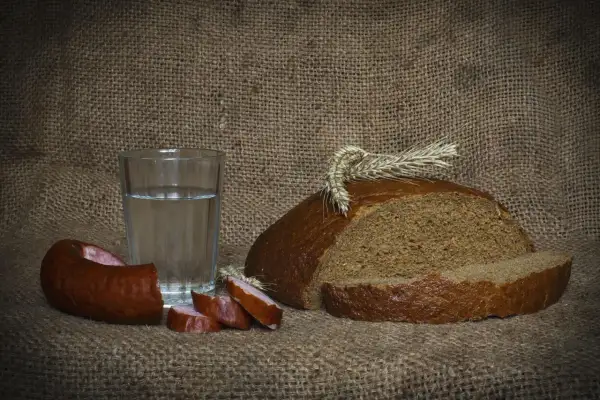 Szklanka wódki z ziemniaka, kromka chleba i kiełbasa na płóciennym tle. Proste, polskie smaki.