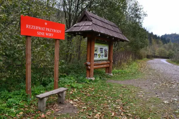 Tablica informacyjna w rezerwacie przyrody Sine Wiry. Drewniana wiata z mapą szlaków i ławka zapraszają do odpoczynku przed leśną wędrówką.