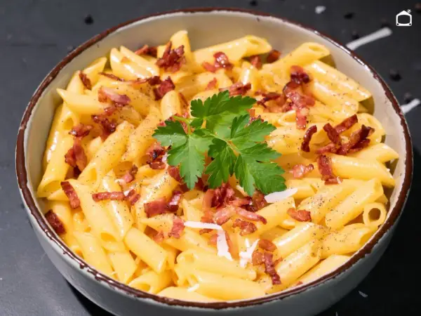 Un tazón de macarrones a la carbonara, cubiertos con trozos de tocino crujiente, perejil fresco y pimienta negra.