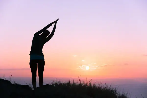 Silueta de una persona en postura de yoga al amanecer, sintiendo la energía vital del nuevo día.
