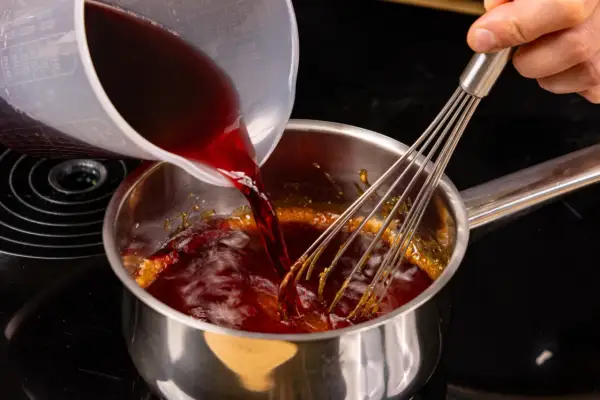 Flüssigkeit wird in einen Topf mit karamellisiertem Zucker gegossen, während ein Schneebesen umrührt, um eine Balsamico-Creme herzustellen.