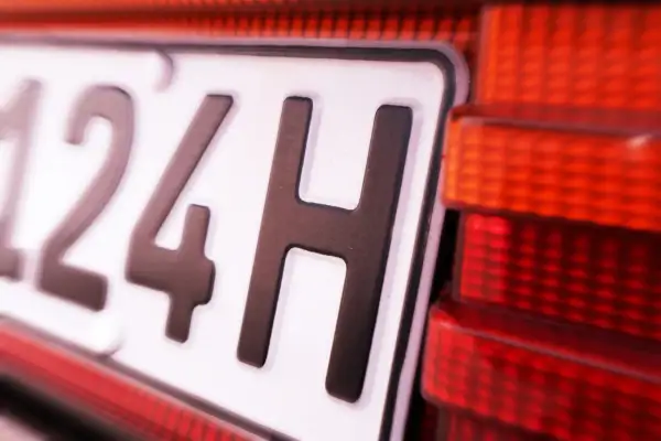 Nahaufnahme eines Nummernschilds mit der Aufschrift "124H". Daneben ist ein rotes Rücklicht zu sehen. Vielleicht eine Geschwindigkeitsbegrenzung?