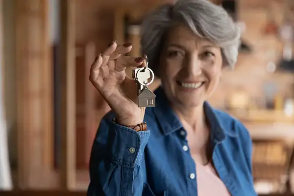 Une femme souriante de plus de 65 ans tient des clés avec un pendentif maison. Elle bénéficie de la **loi alur locataire plus de 65 ans**.