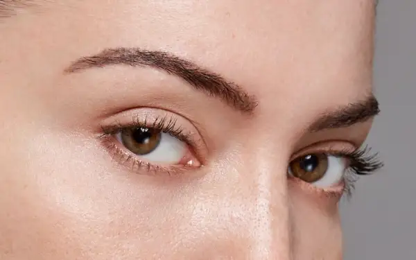 Gros plan sur des yeux marron avec des cils longs. Le sourcil gauche est légèrement plus fin, montrant comment dessiner ses sourcils pour un look naturel.