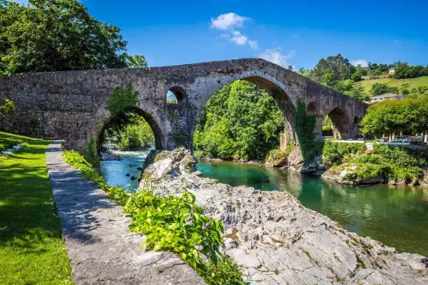 El histórico puente de Cangas de Onís cruza un río de aguas cristalinas rodeado de exuberante vegetación.