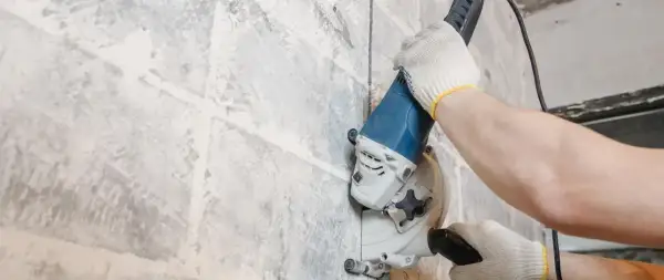 Mani guantate usano una fresatrice per creare un solco nel muro, un metodo per capire se ci sono tubi nascosti.
