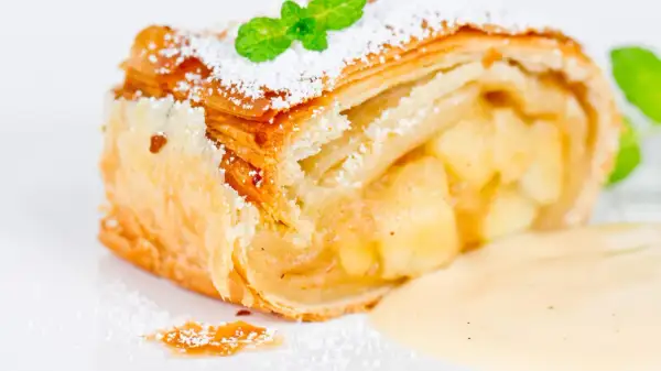 Ein Stück Apfelstrudel mit Puderzucker und Minze, serviert mit Vanillesauce.
