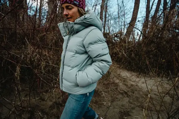 Kobieta w jasnoszarej, puchowej kurtce z kapturem Columbia Puffect Jacket spaceruje po leśnej ścieżce.