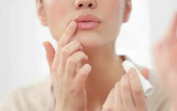 Mujer aplicándose bálsamo labial para el cuidado de labios.