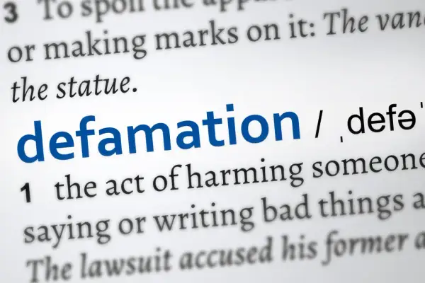 Słownikowa definicja "defamation" (zniesławienia), opisująca szkodzenie komuś przez mówienie lub pisanie złych rzeczy. Uważaj na pomówienia w pracy.