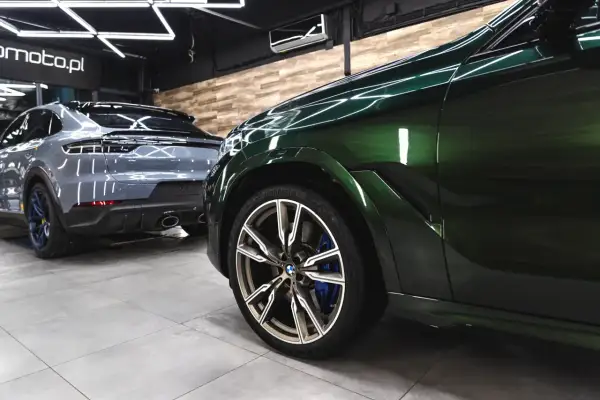 Błyszczące, zielone BMW i szare Porsche w studio auto detailing. Lśniące felgi i perfekcyjnie wypolerowane karoserie świadczą o profesjonalnej pielęgnacji.