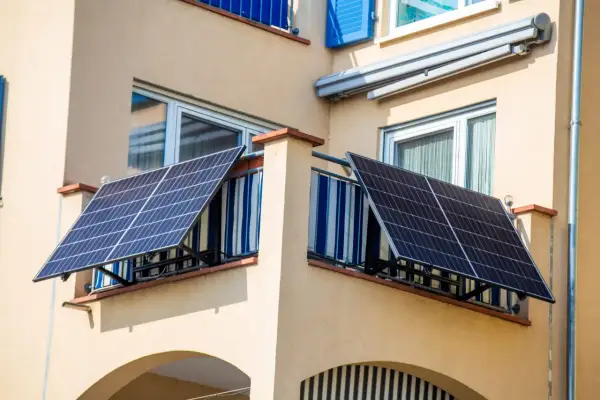 Due pannelli solari da balcone catturano l'energia del sole, montati su una ringhiera con tende a righe blu e bianche.