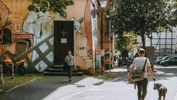 Ein Mann geht mit Hund durch eine Straße in Wuppertal, vorbei an einer Wand mit Graffiti.