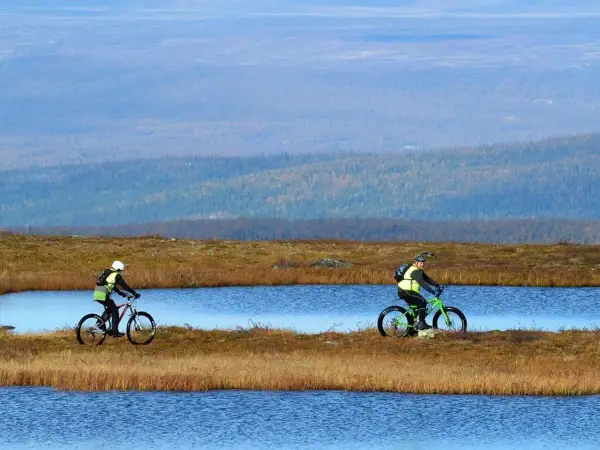 Två cyklister njuter av en cykelsemester i Sverige, susar fram längs sjöar i ett vidsträckt landskap.