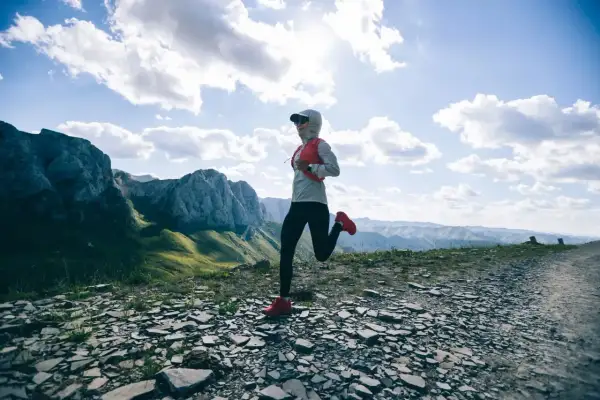 Une coureuse s'élance sur un sentier rocailleux, dominant des montagnes majestueuses. Un paysage digne d'un trail mythique en France.