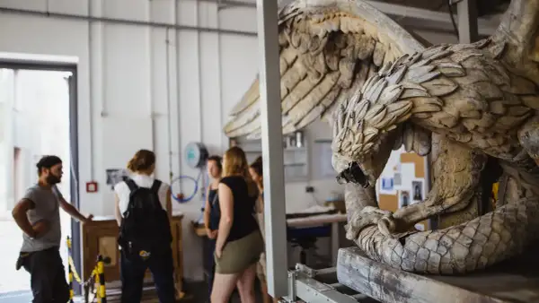 Studierende im Restaurationsstudium betrachten eine detailreiche Skulptur eines geflügelten Wesens.