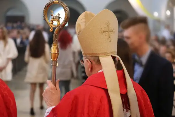Biskup w czerwonej szacie i mitrze z krzyżem, trzyma pastorał ze złotym barankiem.