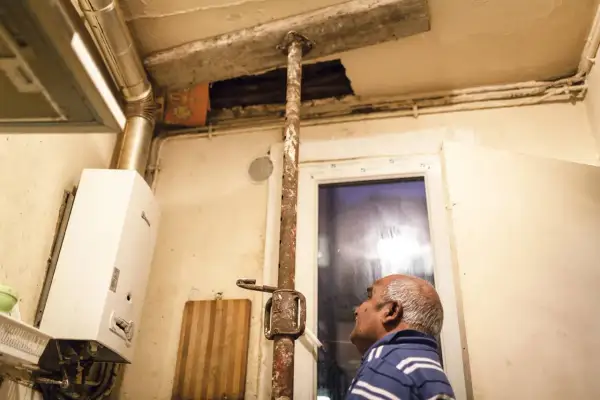 Un homme regarde un plafond délabré soutenu par une poutre rouillée. Ce **logement insalubre** montre des signes de dégradation avancée.